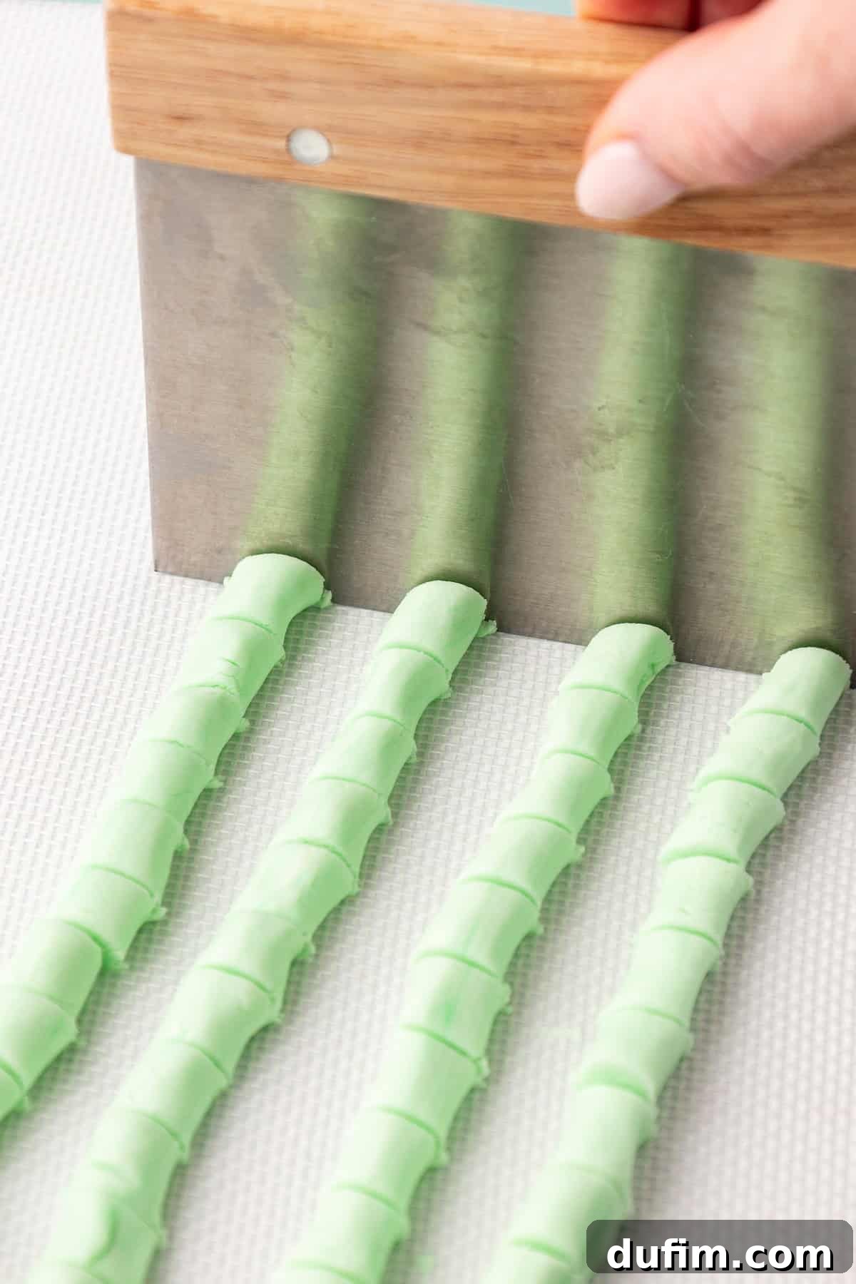 Melt-In-Your-Mouth Butter Mints 16 A sharp knife or bench scraper is used to cut four rows of green butter mint dough ropes into uniformly small, bite-sized pieces on a clean surface.