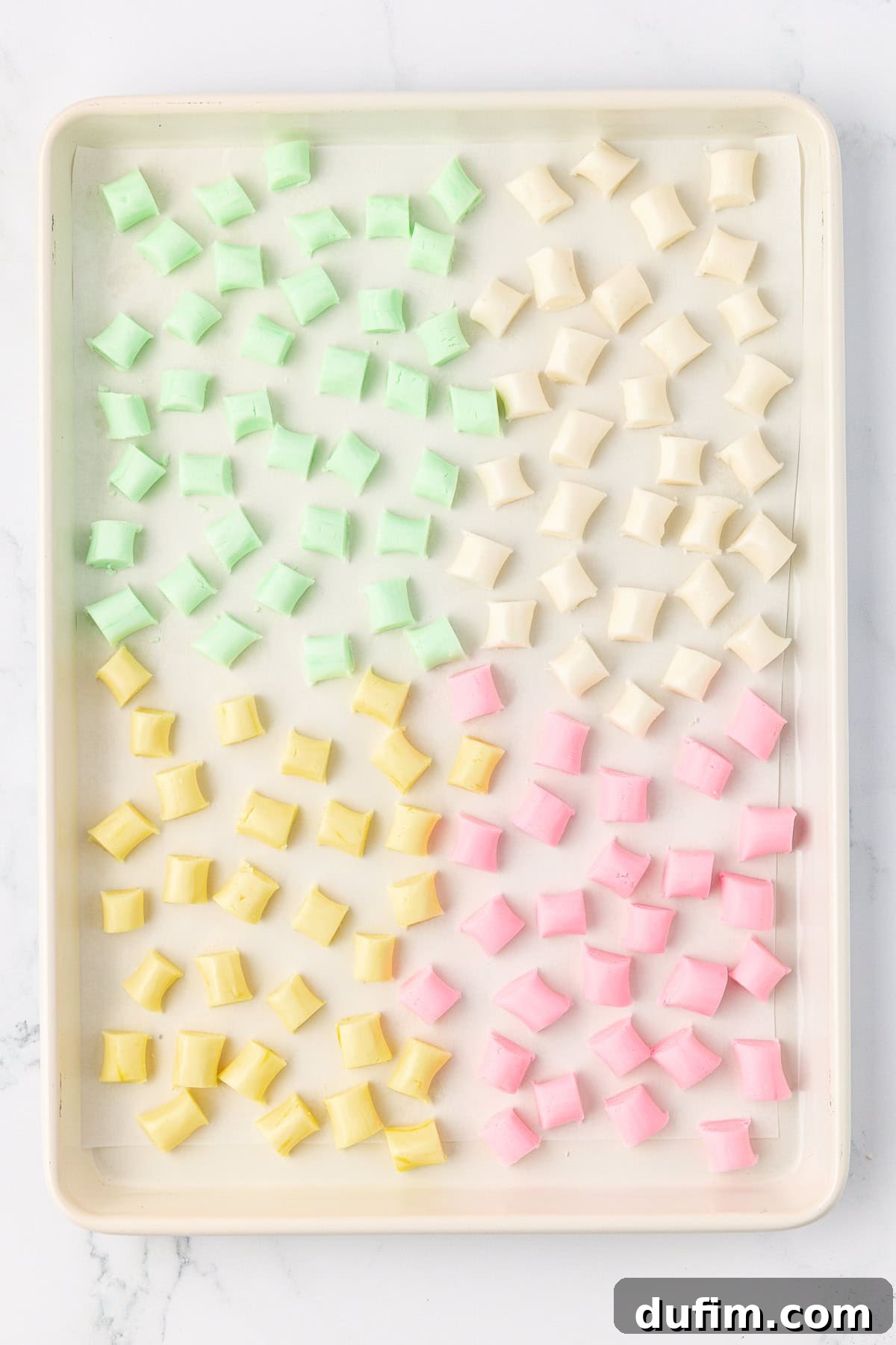 Melt-In-Your-Mouth Butter Mints 17 An overhead view of a sheet pan displaying an array of green, white, yellow, and pink butter mints neatly spread out and air-drying.