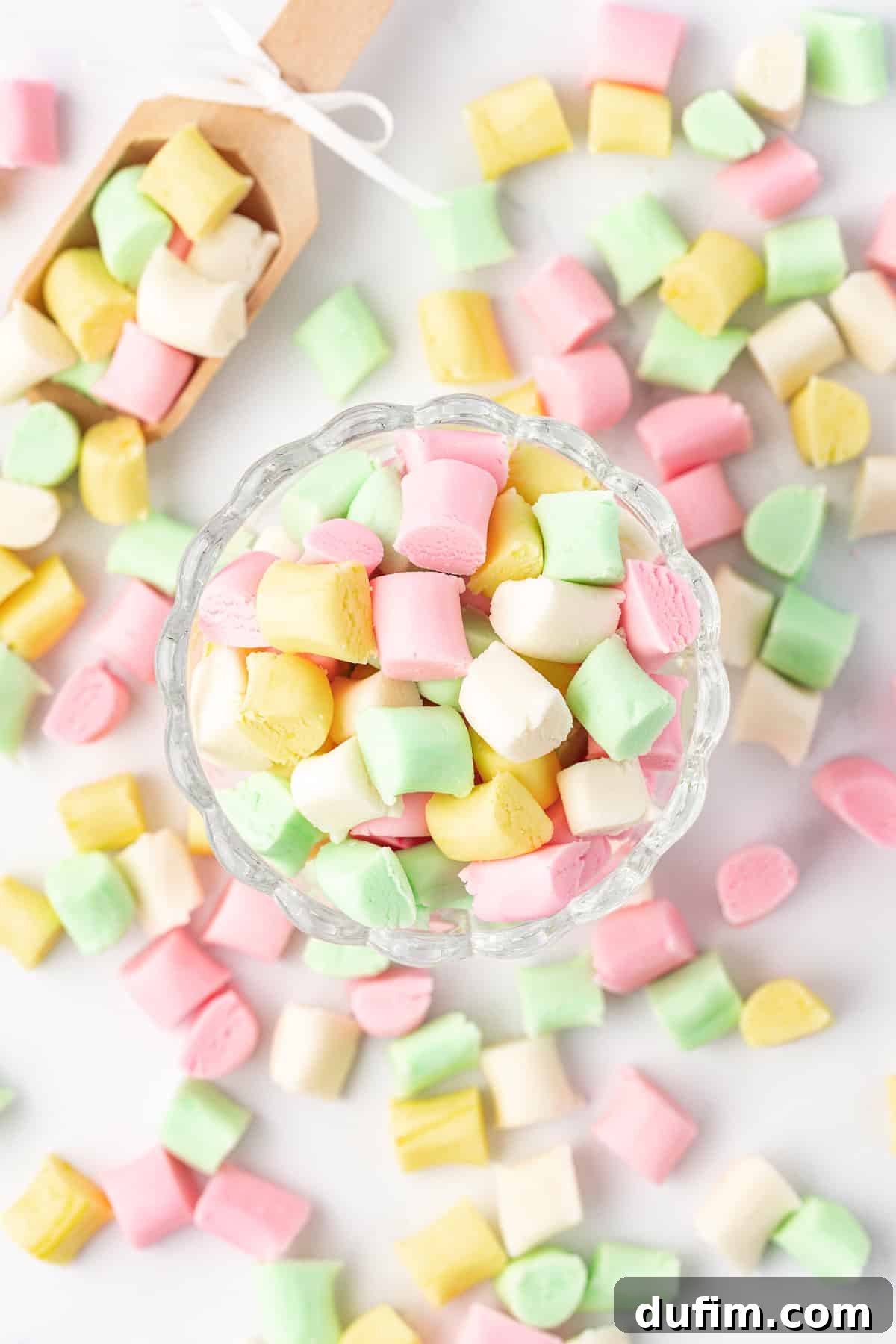 Melt-In-Your-Mouth Butter Mints 18 An overhead view of a charming small glass dish overflowing with an assortment of butter mints, with more mints casually scattered around its base.
