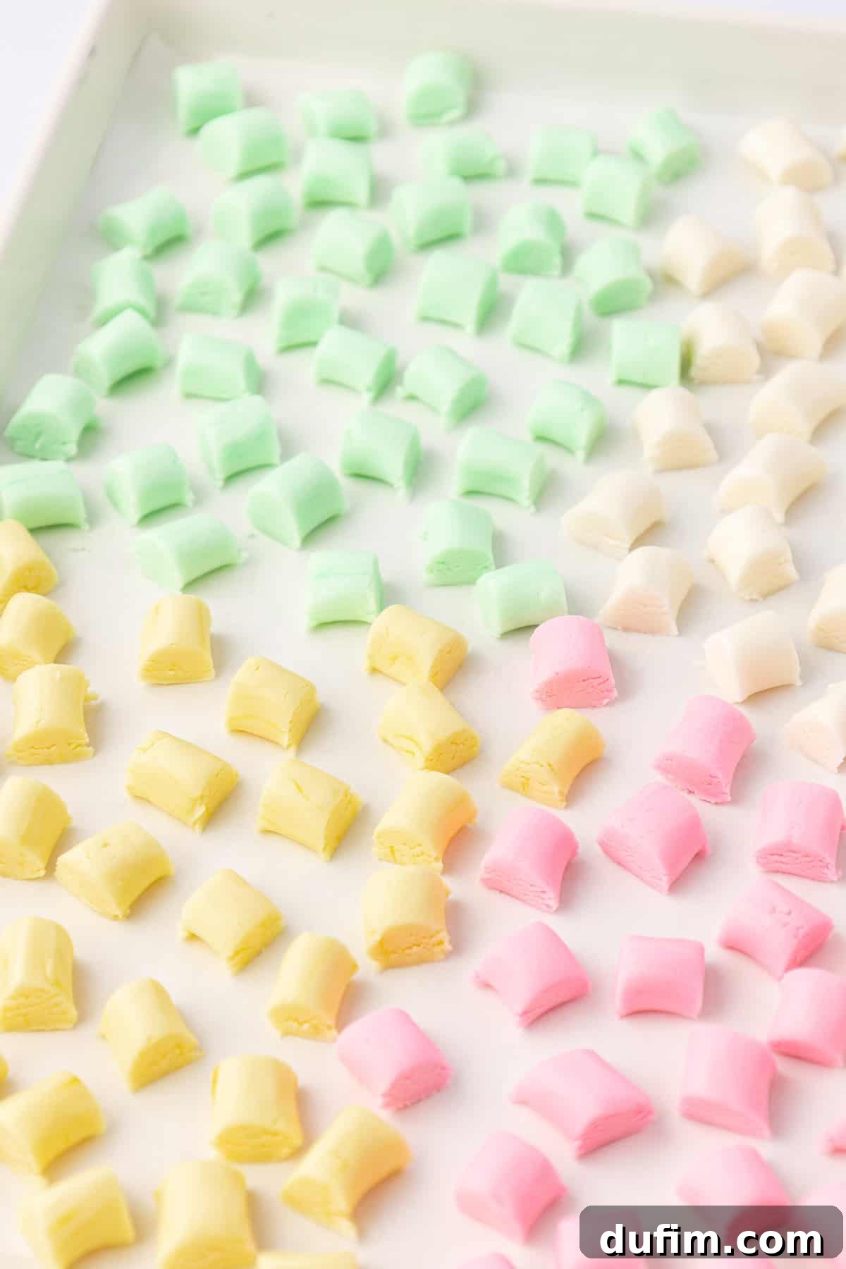 Melt-In-Your-Mouth Butter Mints 19 A baking sheet neatly arranged with yellow, green, white, and pink butter mints, spread in a single layer for drying.
