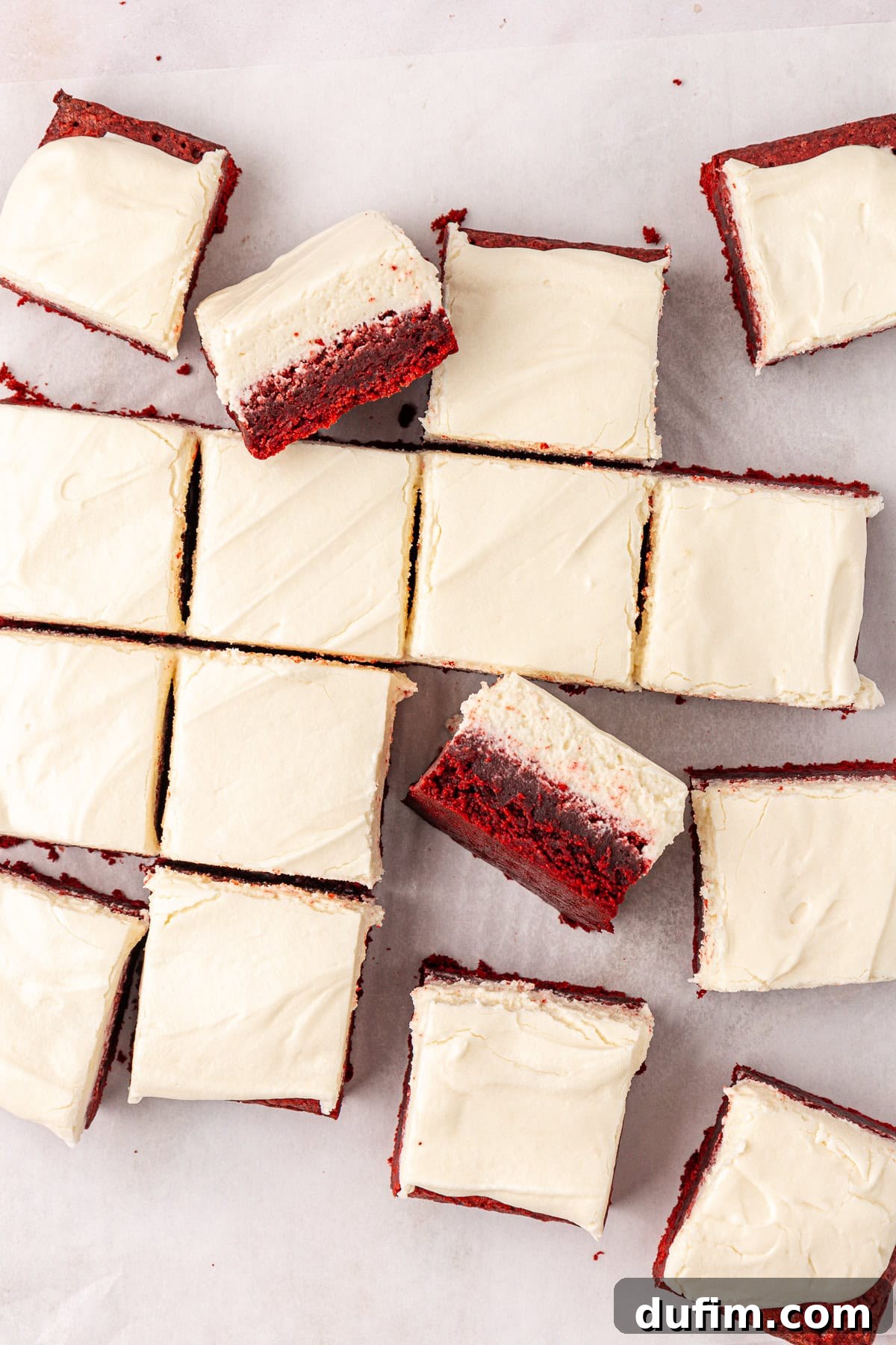 overhead view of scattered red velvet brownies topped with cream cheese frosting, some in rows, some leaning on others and some on their sides showing the two layers of brownie and frosting