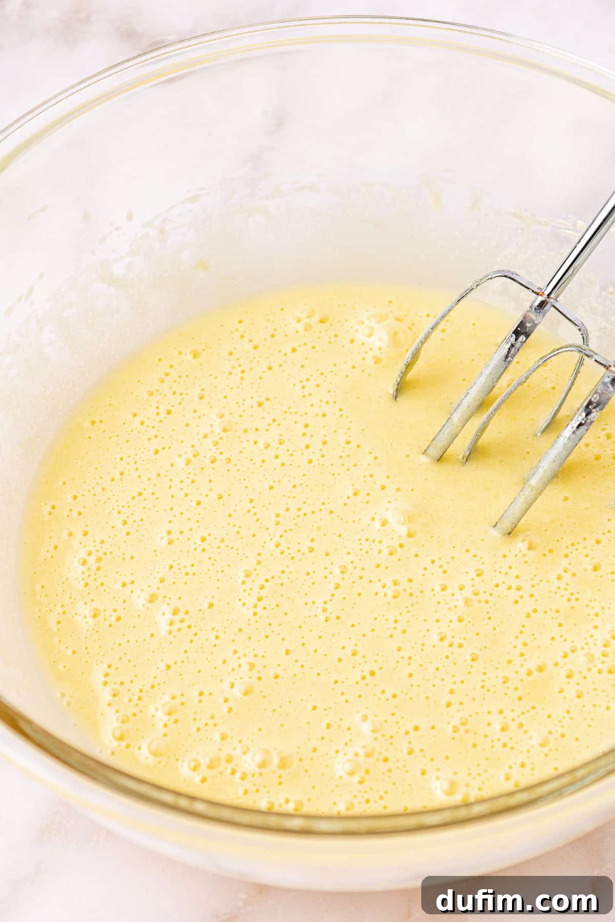 wet ingredients for red velvet brownies in a clear glass bowl with electric mixers leaning on the inside of the bowl