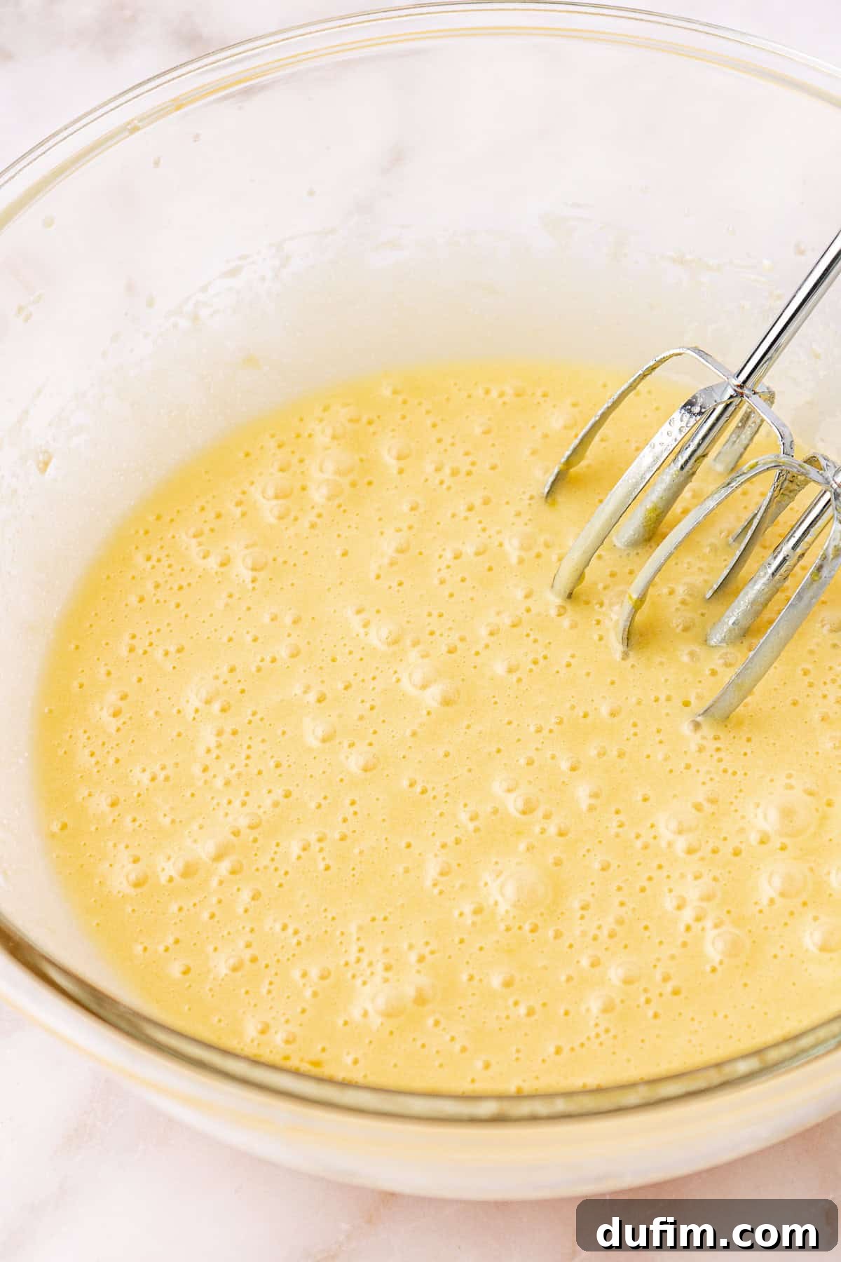 wet ingredients for red velvet brownies in a clear glass bowl with electric mixers leaning on the inside of the bowl