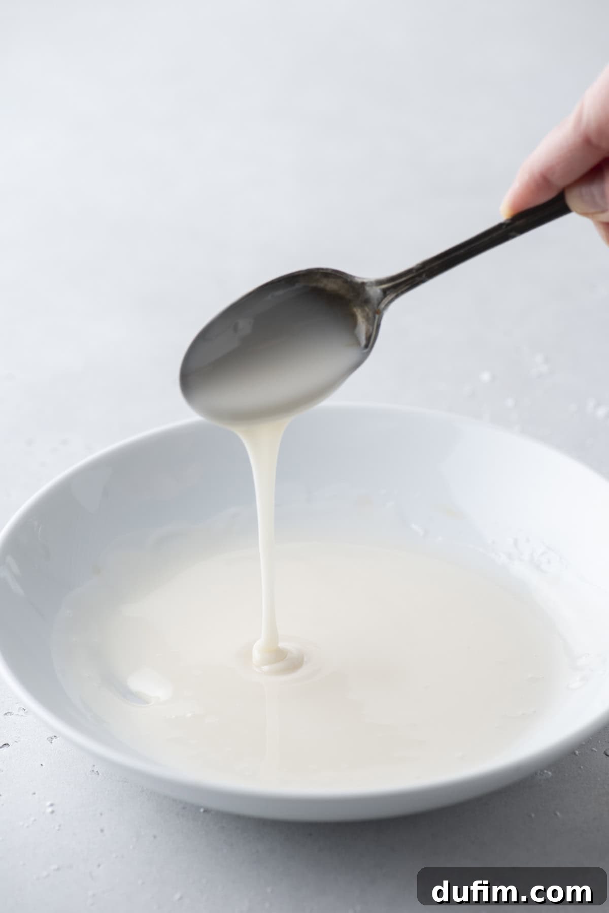 Effortless Donut Glaze Perfection 2 Silky smooth donut glaze dripping from a spoon into a white bowl, ready for dipping.