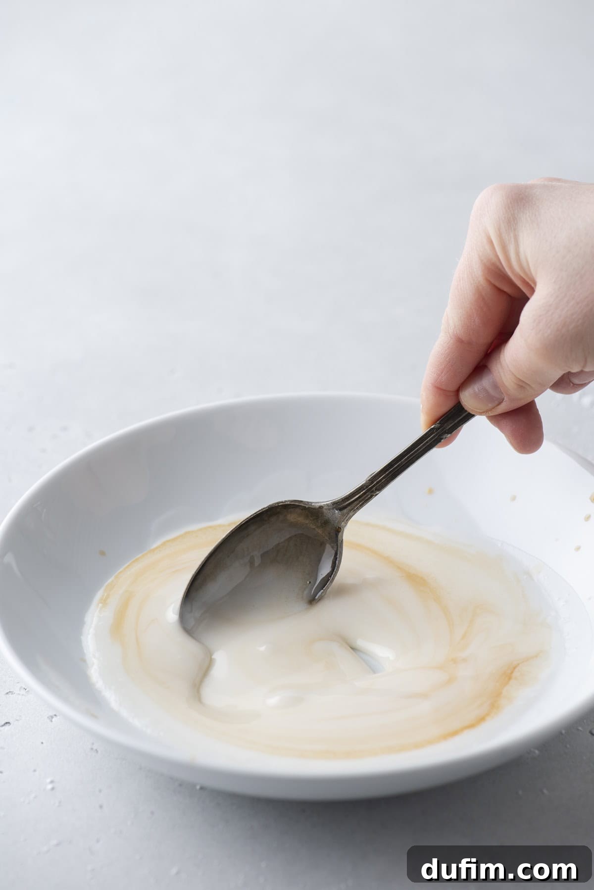 Effortless Donut Glaze Perfection 11 A close-up of vanilla extract being gently stirred into a creamy white donut glaze in a bowl.