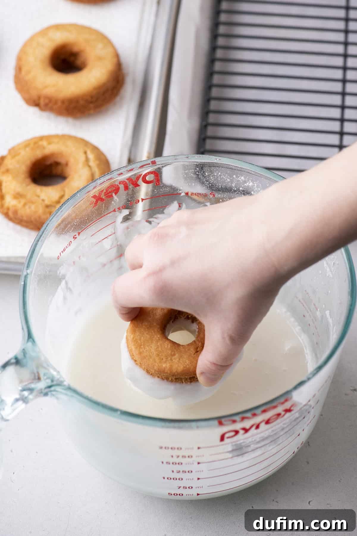 Effortless Donut Glaze Perfection 12 A homemade donut being carefully dipped into a generous amount of vanilla glaze in a measuring cup.