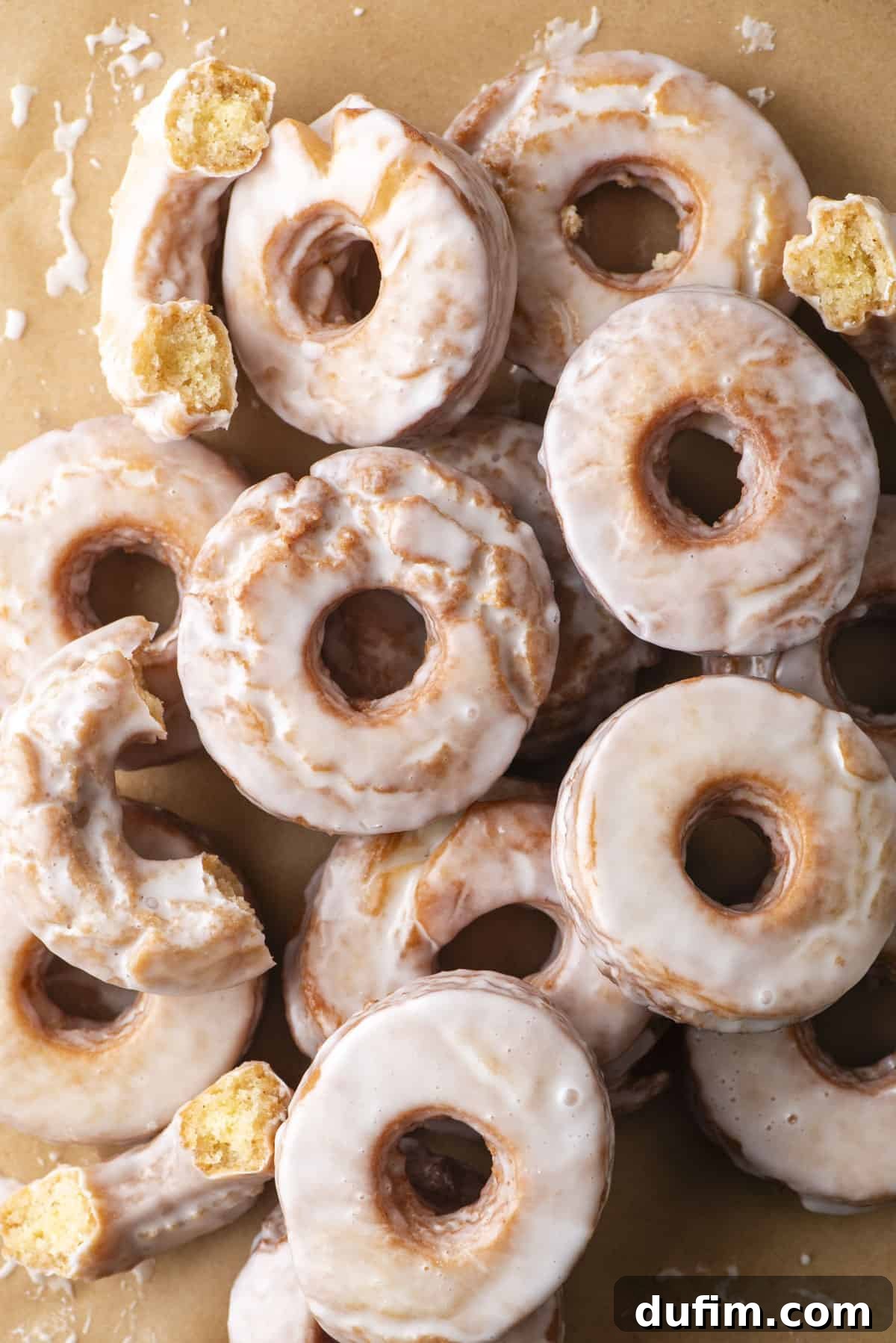 Effortless Donut Glaze Perfection 14 Overhead view of several perfectly glazed donuts artfully arranged on a rustic brown paper surface.