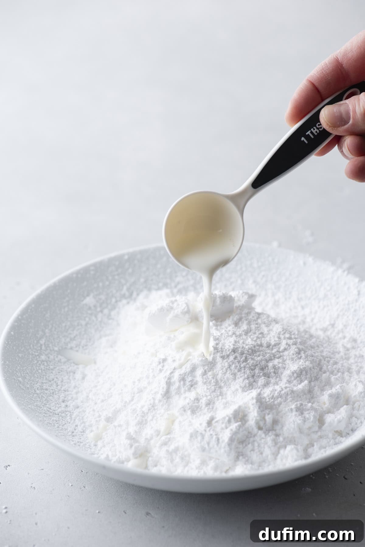 Effortless Donut Glaze Perfection 7 A stream of milk being carefully poured into a bowl of sifted powdered sugar, ready for mixing.