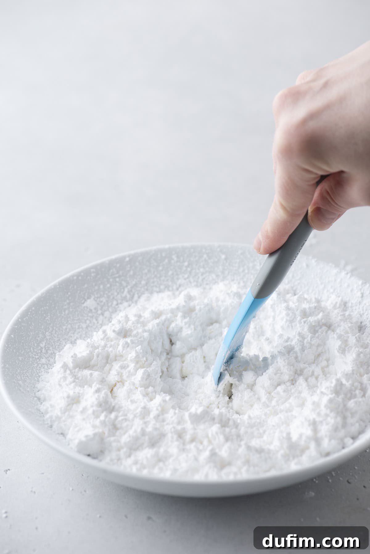 Effortless Donut Glaze Perfection 8 Spatula mixing powdered sugar and milk in a white bowl, forming the smooth donut glaze.