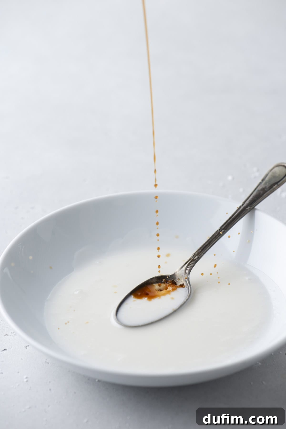 Effortless Donut Glaze Perfection 10 Vanilla extract being added to a bowl of freshly mixed donut glaze, enhancing its aroma and flavor.