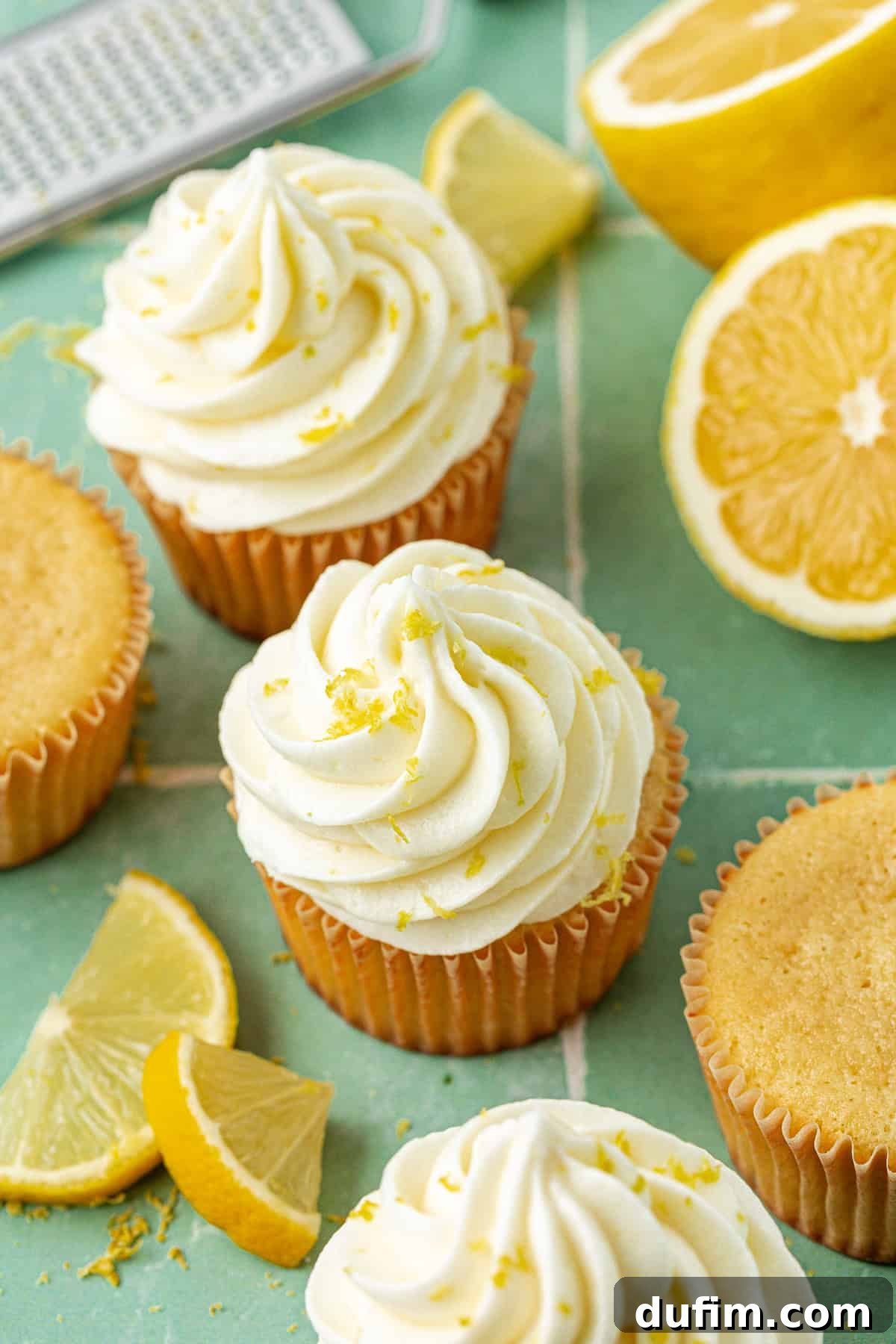 Luscious Lemon Cream Cheese Frosting 12 Assortment of cupcakes generously topped with vibrant lemon cream cheese frosting and sprinkled with fresh lemon zest, artfully arranged around a grater, sliced lemons, and scattered zest, creating a visually appealing and fresh display.