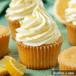 Lemon cream cheese frosting on cupcakes topped with lemon zest surrounded by more zest and lemon slices
