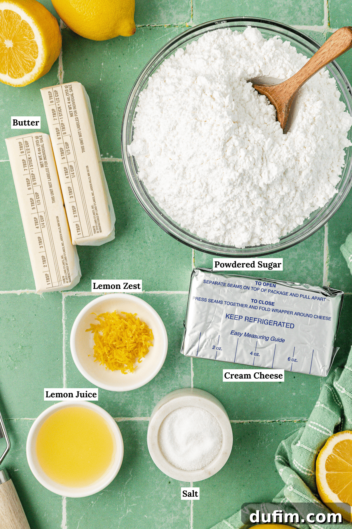 Luscious Lemon Cream Cheese Frosting 4 Overhead view of all fresh ingredients laid out for lemon cream cheese frosting: fresh lemons, powdered sugar, two sticks of unsalted butter, lemon zest, a block of cream cheese, lemon juice in a small glass, and a pinch of salt.