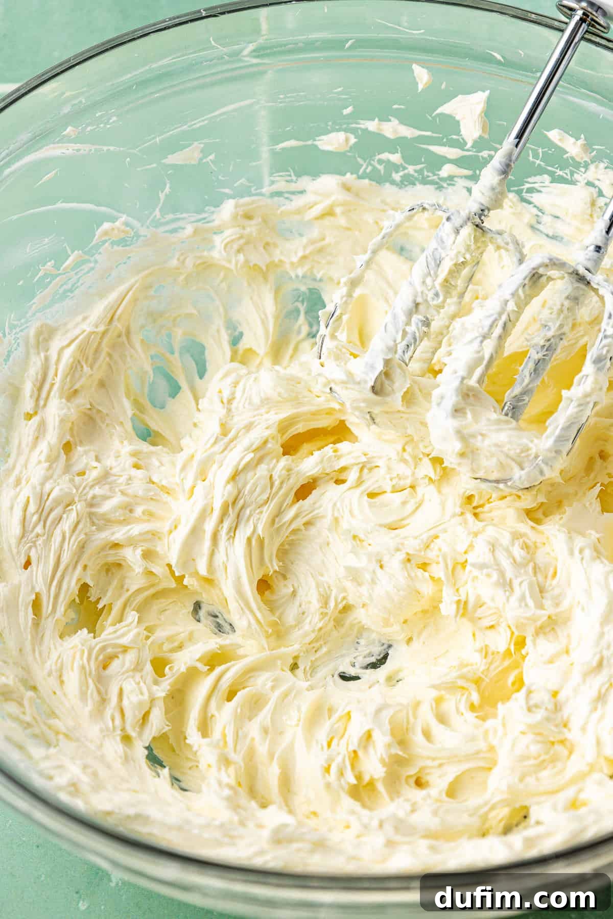 Luscious Lemon Cream Cheese Frosting 7 Softened cream cheese and butter, perfectly creamed together in a large clear glass bowl using an electric mixer, showcasing the light and fluffy consistency.