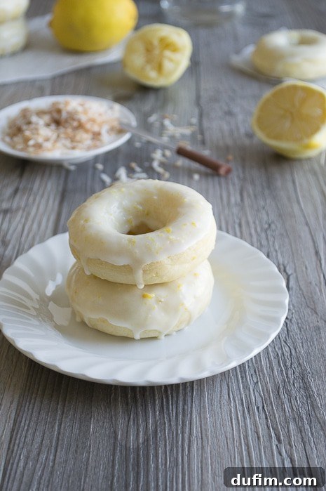 A generous batch of glazed Lemon Coconut Donuts resting on a cooling rack