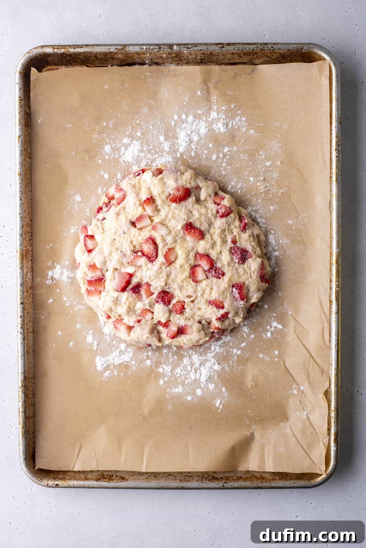 Juicy Strawberry Scones 12 Round scone dough with strawberries on parchment paper-lined baking sheet, dusted with flour.