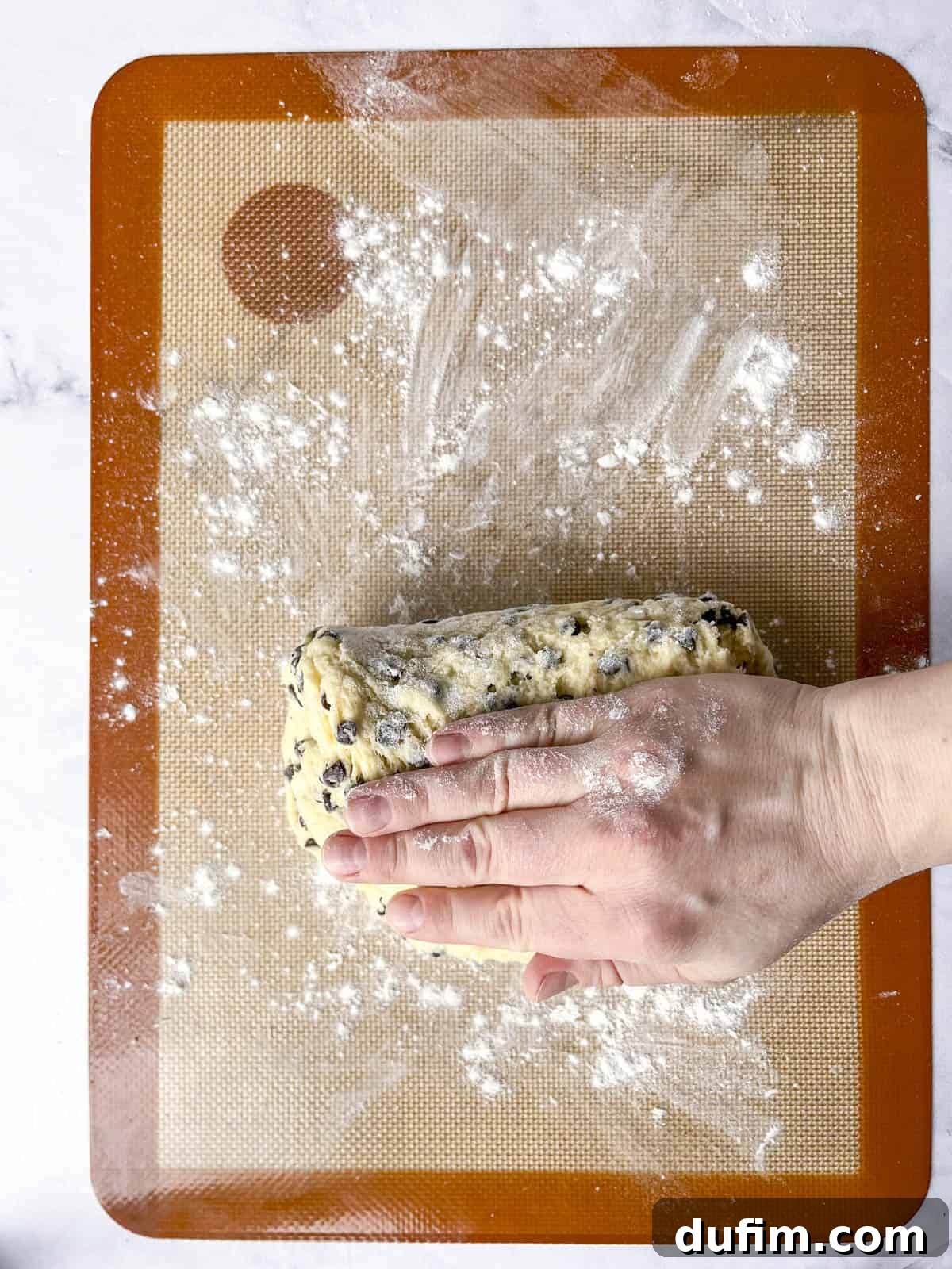 Juicy Strawberry Scones 14 A hand kneads chocolate chip dough on a floured silicone baking mat placed on a marble surface.