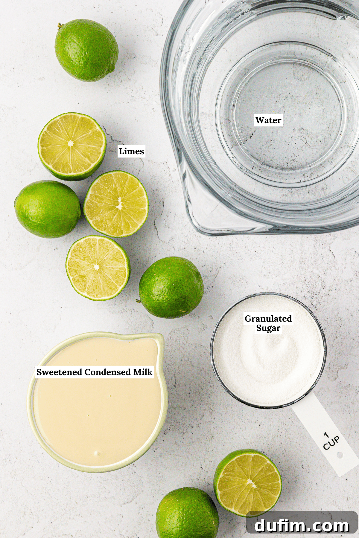 Crafting Creamy Brazilian Lemonade 3 Top-down view of ingredients for brazilian lemonade: a bowl of water, several whole and halved limes, a measuring cup of granulated sugar, and a bowl of sweetened condensed milk on a white surface. Labels identify each item.