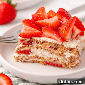 No-Bake Strawberry Dream 17 A slice of layered strawberry dessert with whipped cream and graham crackers, topped with fresh strawberry pieces, served on a white plate with a fork.