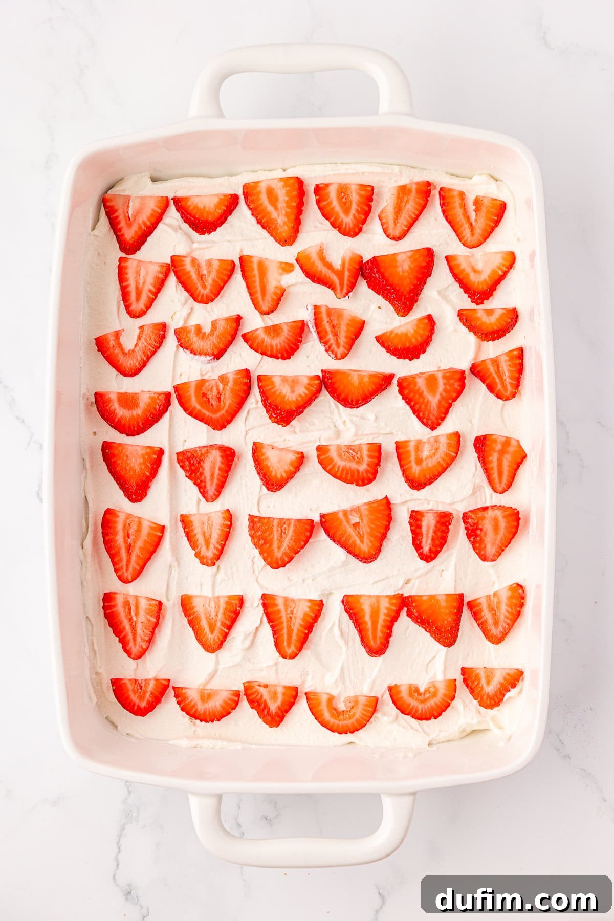 No-Bake Strawberry Dream 10 A white rectangular baking dish filled with a dessert topped with rows of halved fresh strawberries arranged neatly on a layer of white cream.
