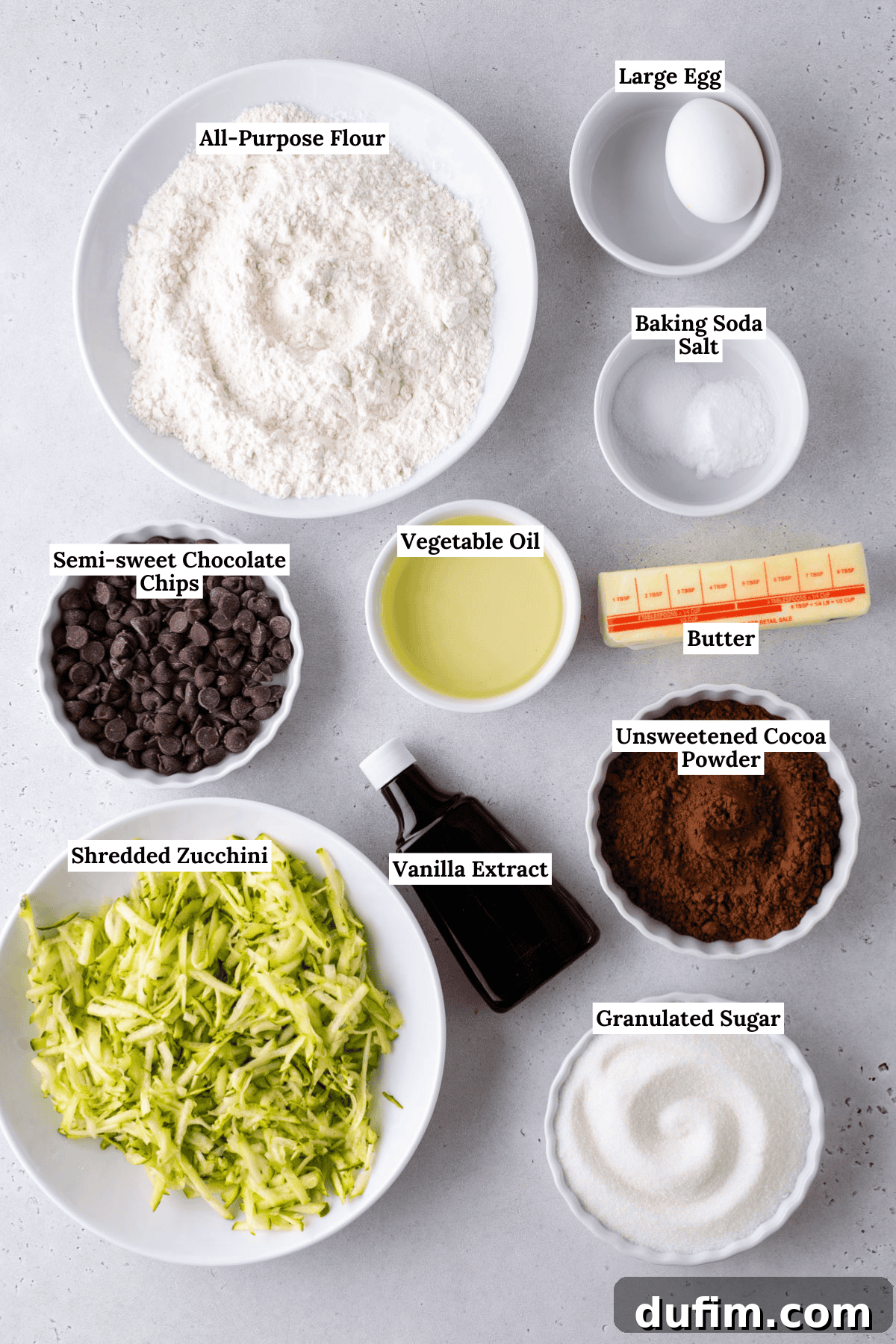 Hidden Harvest Brownies 5 Top-down view of labeled baking ingredients in bowls and plates, including flour, egg, baking soda, salt, butter, cocoa powder, granulated sugar, vegetable oil, vanilla extract, shredded zucchini, and chocolate chips.