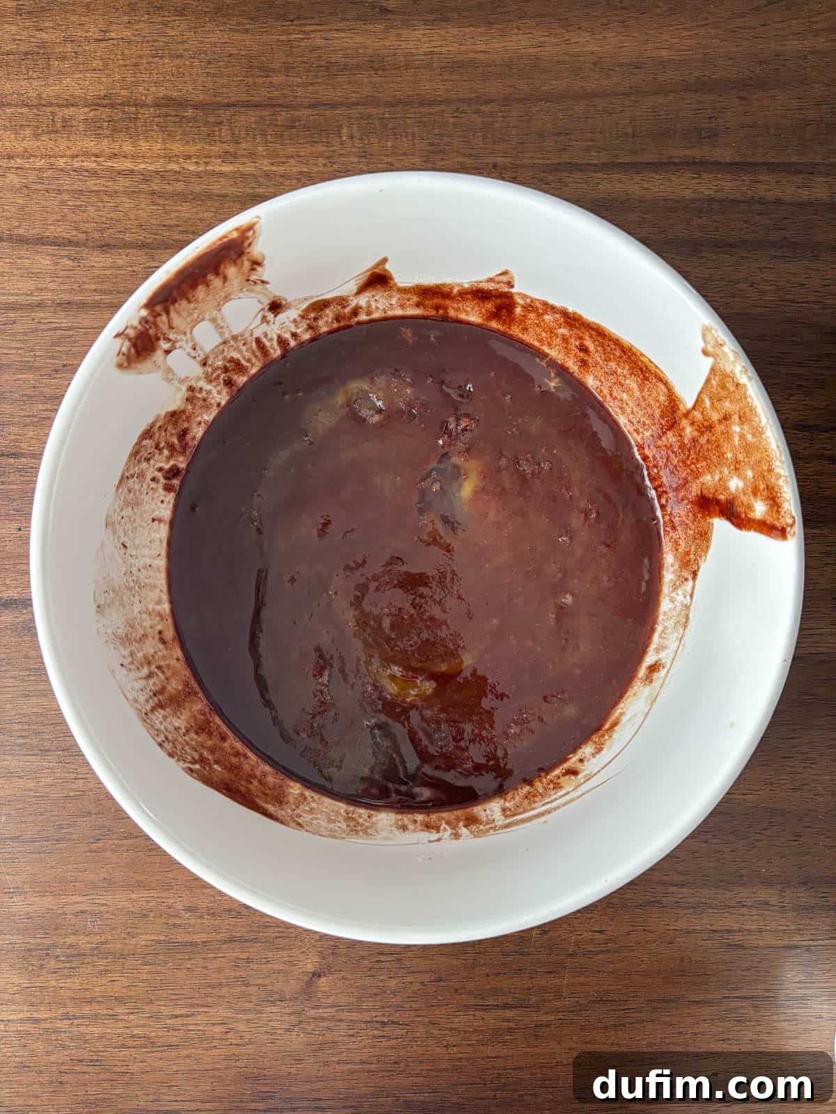 Hidden Harvest Brownies 9 A white bowl filled with dark brown, thick soup or stew sits on a wooden table, with some of the liquid splashed on the rim and side of the bowl.