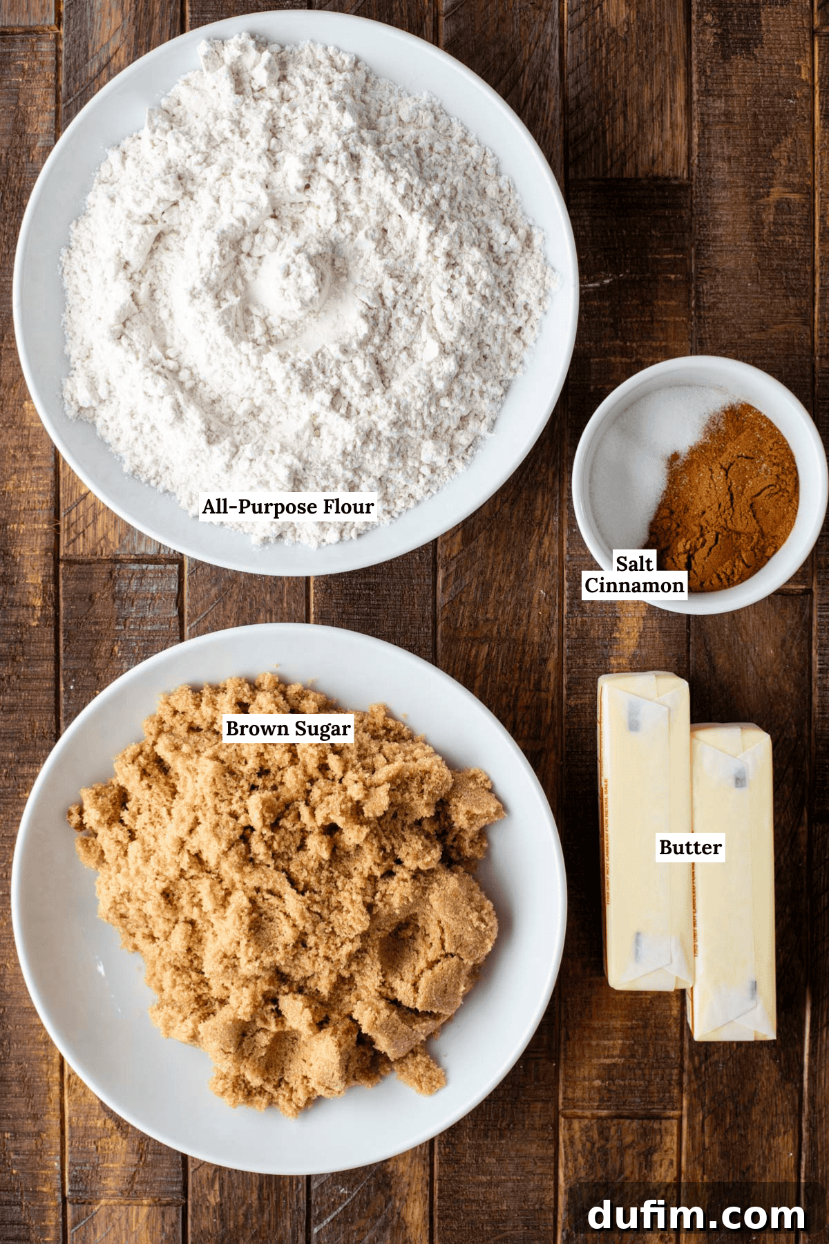 Apple Cinnamon Streusel Coffee Cake 5 Overhead view of measured baking ingredients on a wooden surface: a bowl of all-purpose flour, a small bowl with salt and cinnamon, a plate of brown sugar, and two sticks of butter. Each item is labeled.