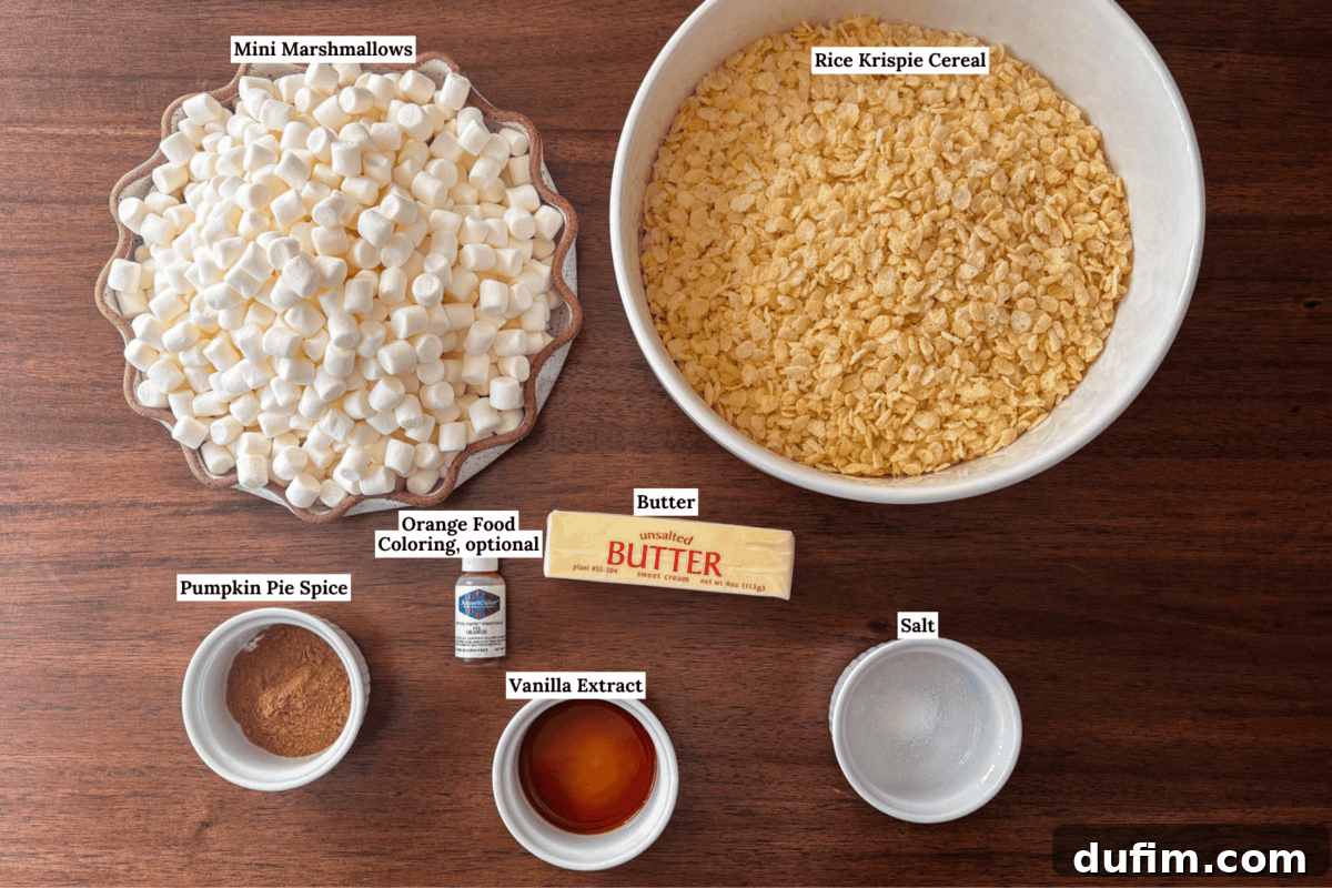 Ingredients for a recipe on a wooden table: a bowl of mini marshmallows, a bowl of Rice Krispie cereal, pumpkin pie spice, vanilla extract, butter, salt, and orange food coloring. Each item is labeled.