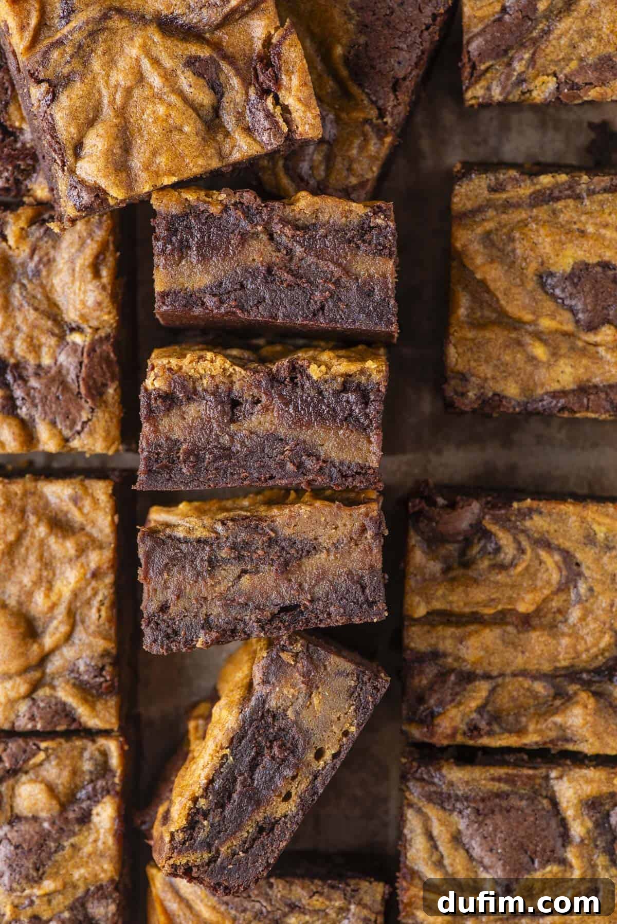 Pumpkin Ripple Fudge Brownies 16 Overhead view of several perfectly cut pumpkin swirl brownies, arranged into neat squares. The brownies showcase a beautiful marbled pattern with rich brown chocolate and vibrant orange pumpkin swirls visible on their tops and sides, inviting a closer look.