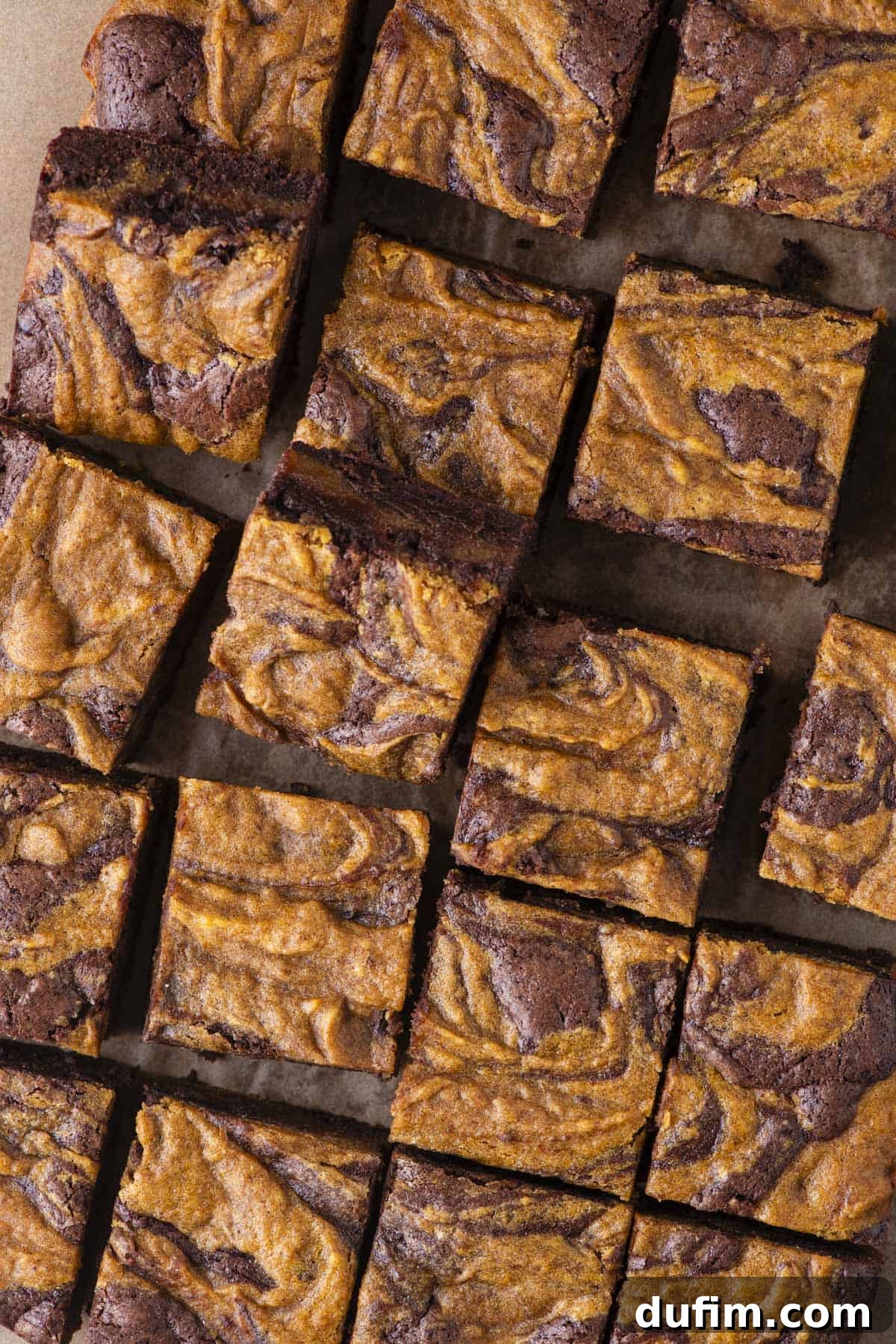 Pumpkin Ripple Fudge Brownies 19 Close-up of several square pieces of brownies with a marbled swirl pattern of dark chocolate and vibrant orange pumpkin batter on top, arranged in neat rows on parchment paper, ready to be picked up and enjoyed.