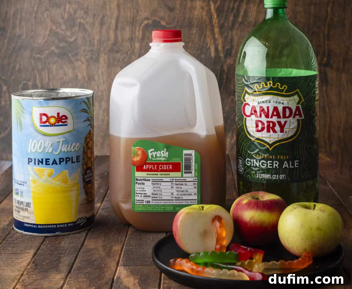 A flat lay arrangement featuring the main ingredients for the punch: a can of Dole pineapple juice, a clear jug of rich apple cider, and a bottle of Canada Dry ginger ale. Alongside these, a small white plate holds colorful gummy worms and freshly sliced red apples, all resting on a rustic wooden surface with a complementary wood-textured background, highlighting the simplicity of the recipe.