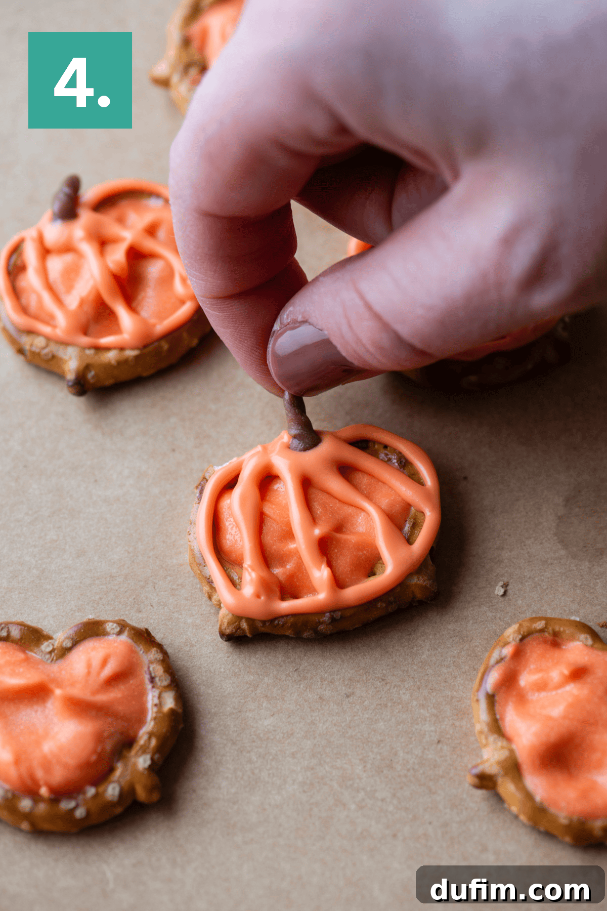 A hand holding a finger over a pretzel with orange frosting.