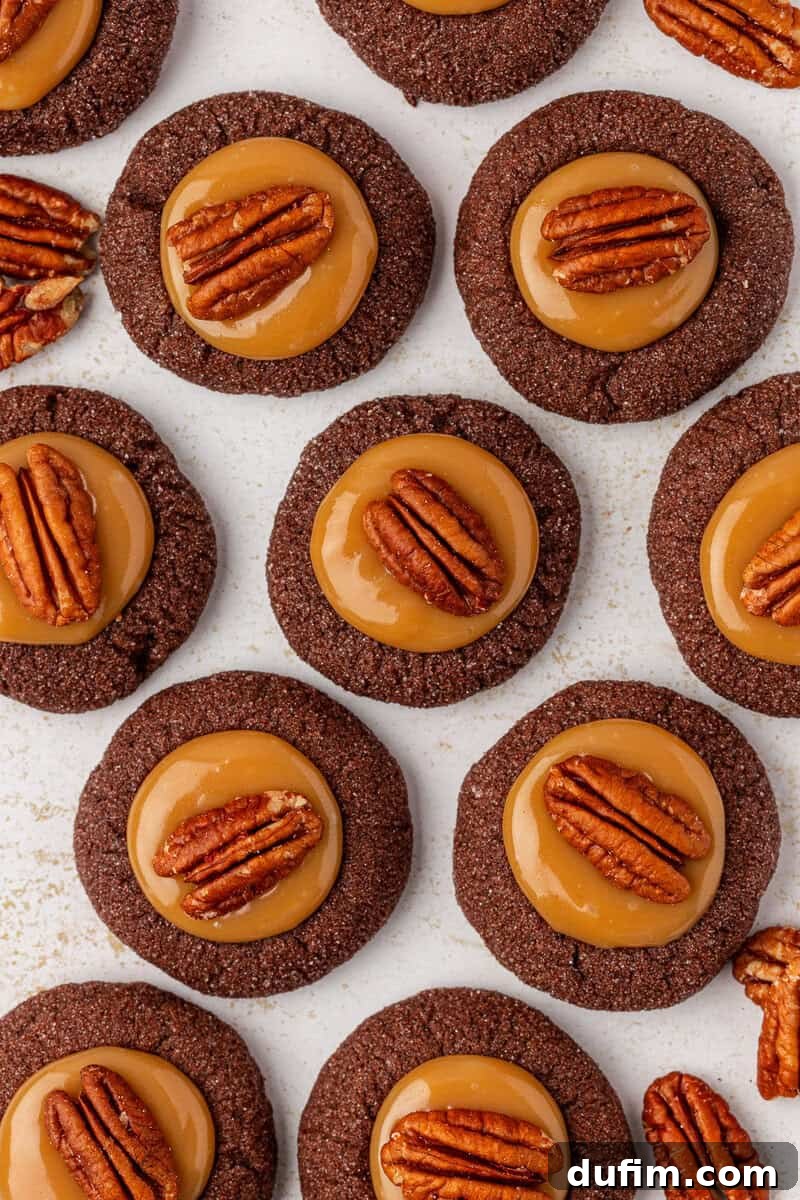 Caramel Pecan Turtle Thumbprints 3 Chocolate cookies topped with caramel and a pecan half are arranged in neat rows on a light surface, creating a uniform and appetizing pattern.