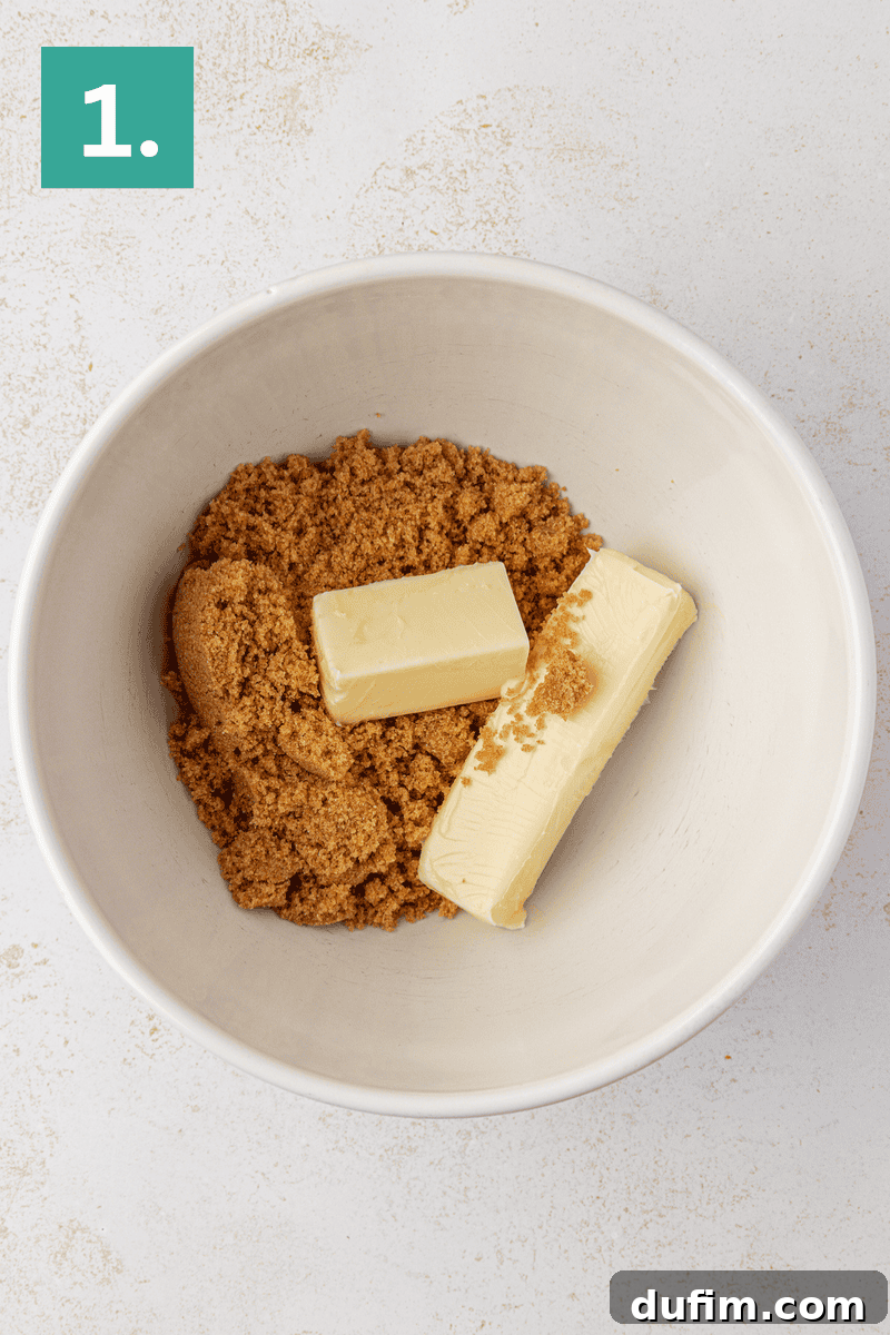 Caramel Pecan Turtle Thumbprints 6 A white bowl contains two sticks of butter and brown sugar. In the top left corner, a green square with the number 1 is displayed. The bowl is set on a light-colored surface.
