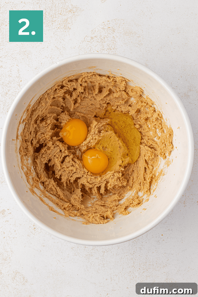 Caramel Pecan Turtle Thumbprints 7 A white mixing bowl with creamed brown sugar and butter mixture, two raw eggs on top, shown from above on a light surface. A green box with the number 2 is in the top left corner.