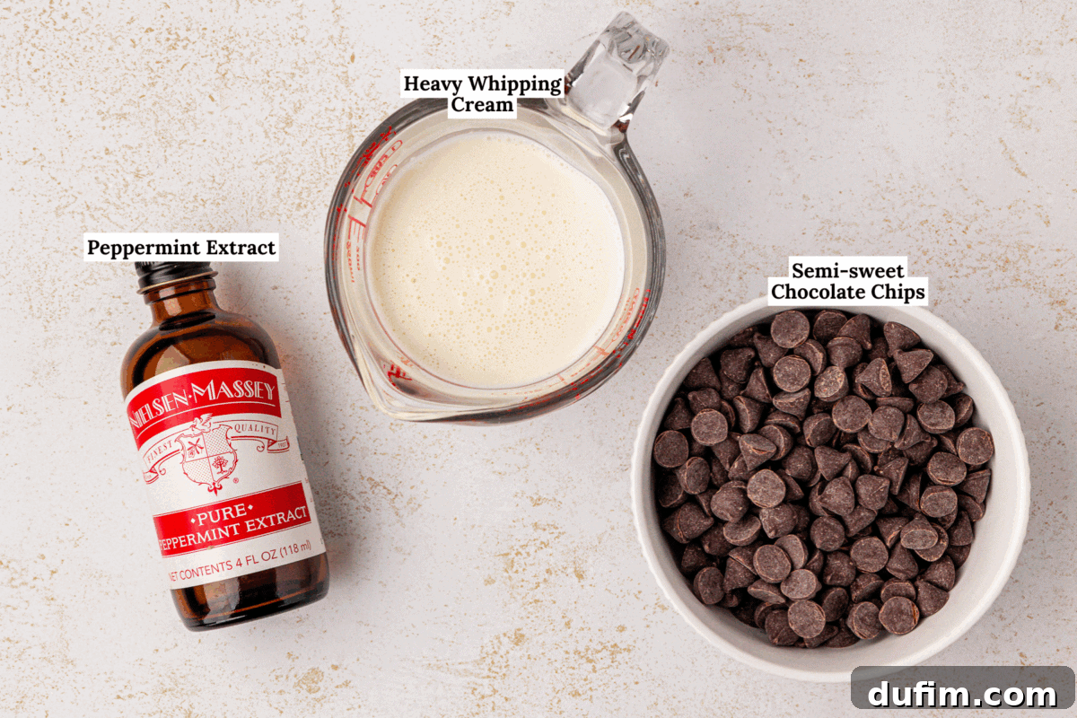 Peppermint Kissed Chocolate Thumbprint Cookies 5 A bottle of peppermint extract, a glass measuring cup of heavy whipping cream, and a bowl of semi-sweet chocolate chips are arranged on a light countertop. Each item is labeled.