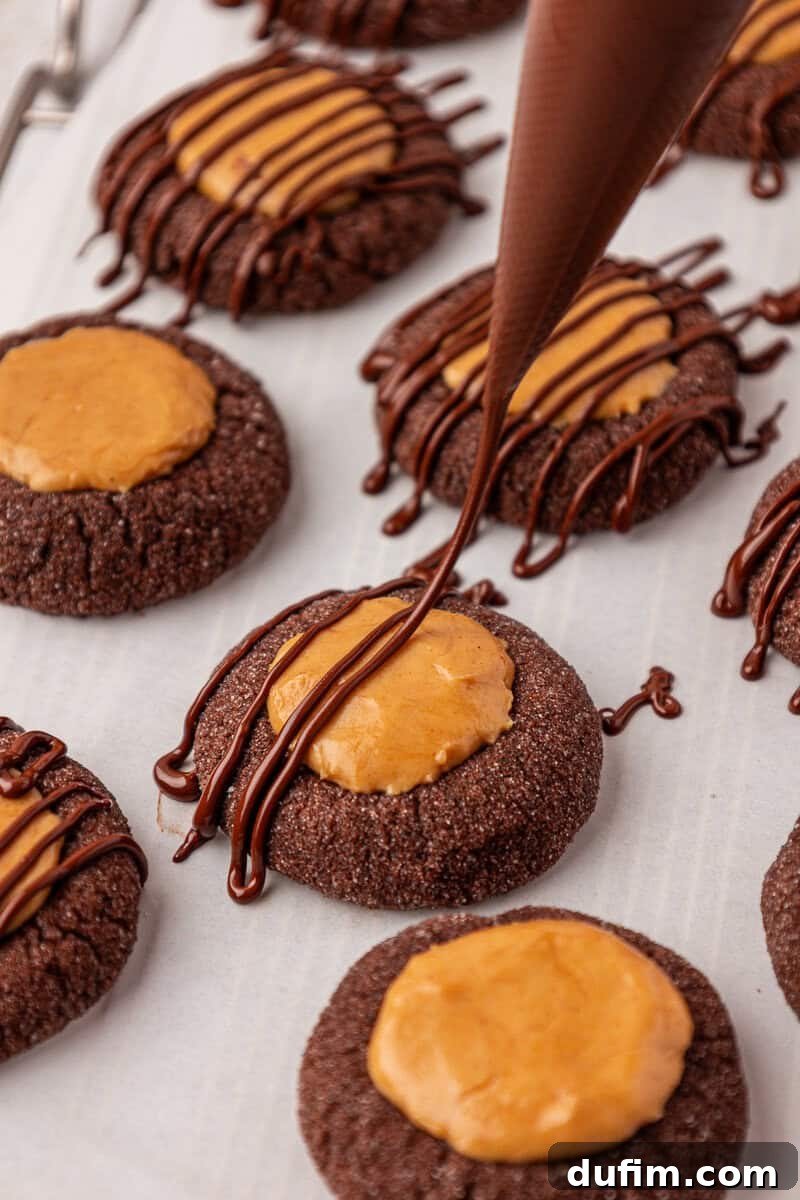 Irresistible Peanut Butter Chocolate Thumbprints 19 Chocolate thumbprint cookies with a peanut butter filling are arranged on parchment paper, while a piping bag is drizzling chocolate over the cookies in the foreground.