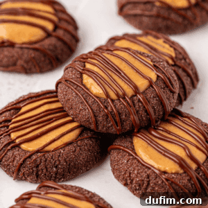 Irresistible Peanut Butter Chocolate Thumbprints 20 Chocolate cookies topped with a dollop of peanut butter and drizzled with melted chocolate, arranged closely together on a white surface.