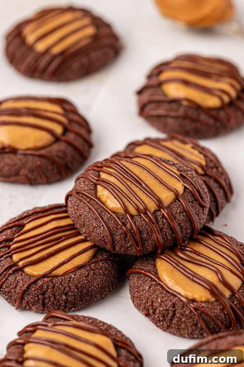 Irresistible Peanut Butter Chocolate Thumbprints 3 Chocolate cookies topped with a peanut butter filling and drizzled with chocolate, arranged on a light surface. The cookies appear soft and rich, with a glossy finish from the chocolate drizzle.
