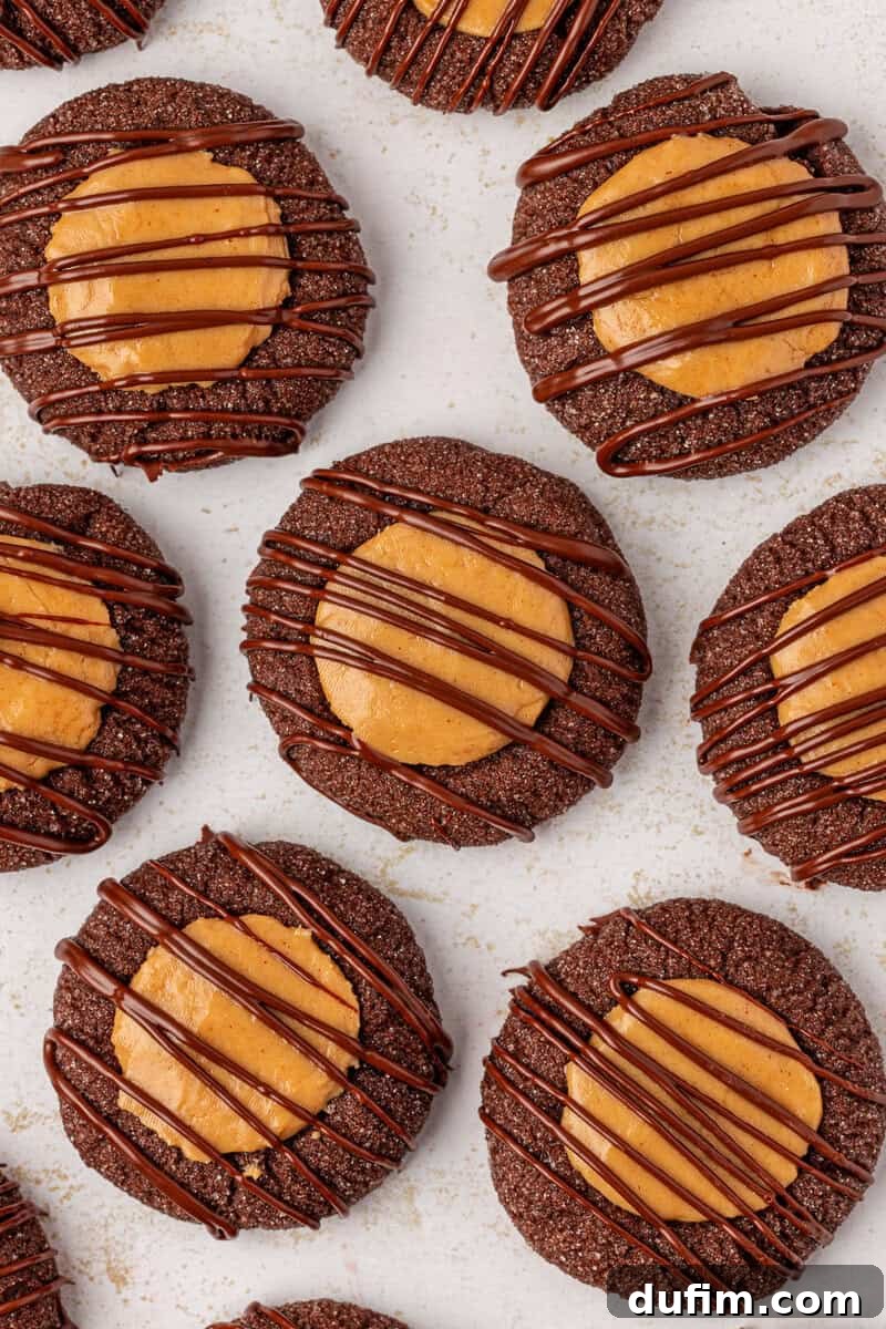 Irresistible Peanut Butter Chocolate Thumbprints 4 Chocolate cookies topped with a round peanut butter center and drizzled with chocolate, arranged closely together on a light-colored surface.