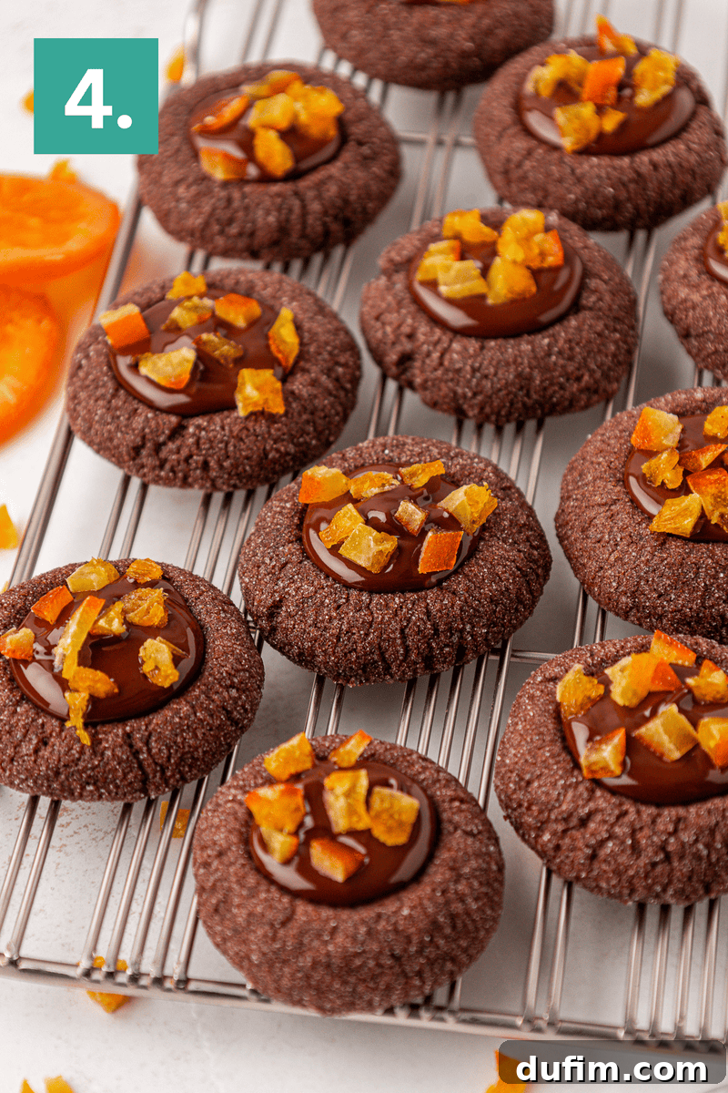 Chocolate thumbprint cookies topped with glossy chocolate ganache and pieces of candied orange sit on a cooling rack. An orange number 4 is displayed in the top left corner.