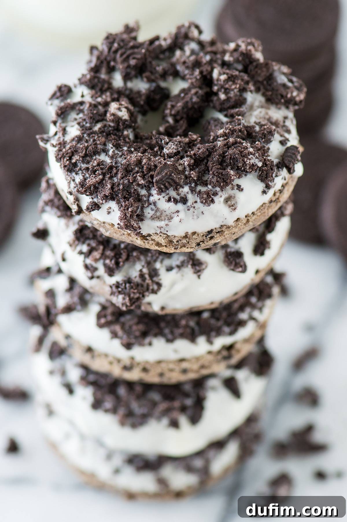 Close-up of a stack of freshly baked Oreo donuts with a creamy white glaze and chunky Oreo pieces.