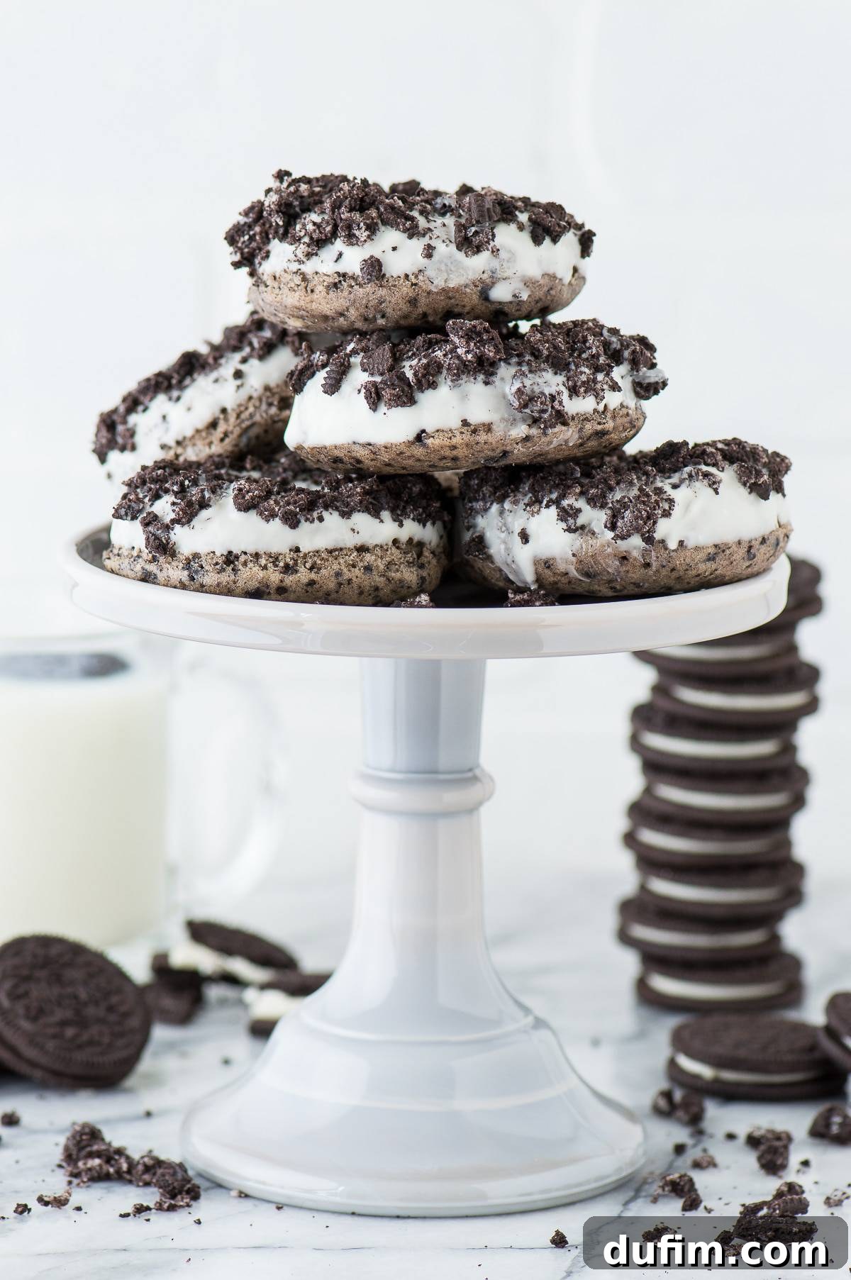 Hand holding a freshly glazed Oreo donut, showing the thick white chocolate and generous Oreo crumb topping.