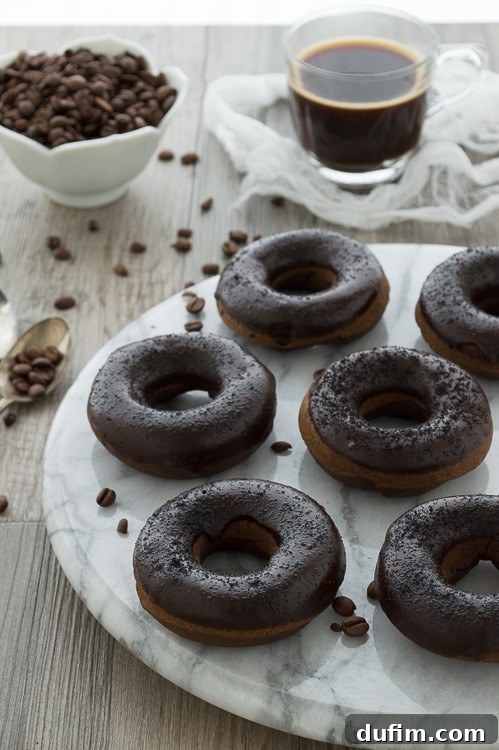 Brewed and Baked Bliss 4 A stack of three glistening coffee donuts, elegantly garnished with whole coffee beans and espresso grounds, emphasizing their rich and authentic coffee flavor.