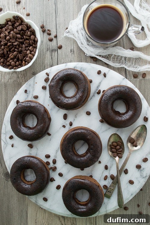 Brewed and Baked Bliss 5 A detailed close-up of a single coffee donut, richly coated in a dark chocolate-coffee glaze and sprinkled with fine espresso grounds, showcasing its irresistible texture and inviting appearance.