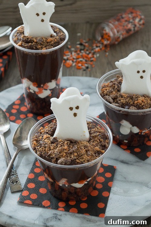 Four Halloween pudding parfaits presented in clear glasses with spooky toppings.