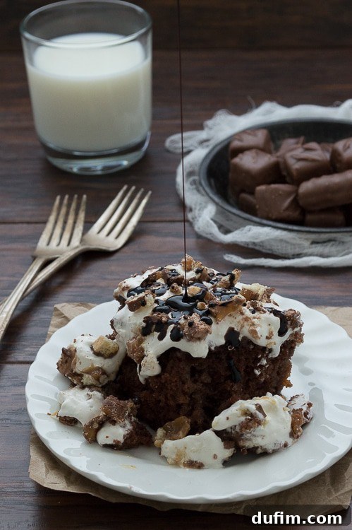 The ultimate Candy Bar Cake in a baking dish, freshly topped with frosting and a generous sprinkle of chopped candy bars, ready for chilling.