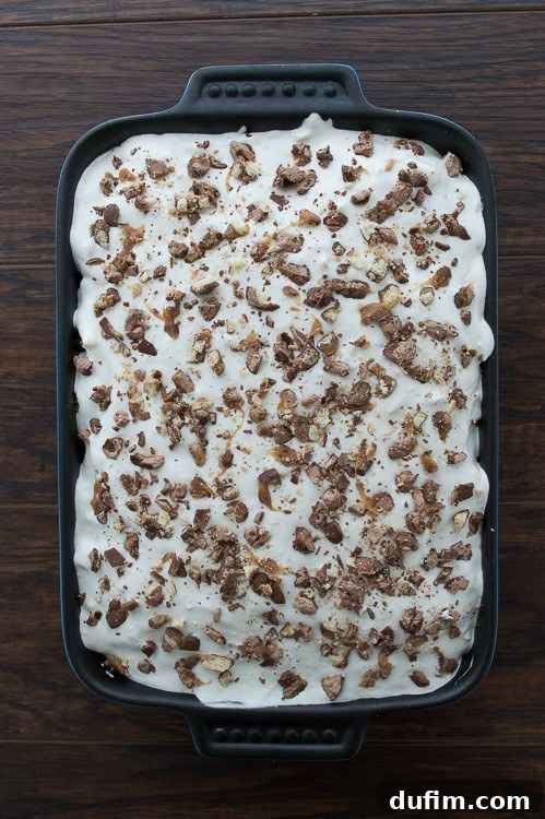 Close-up of the Candy Bar Cake with a generous portion cut out, revealing the moist cake, creamy frosting, and embedded candy pieces.