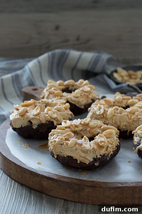 Close-up of a stack of Snickers Donuts, showing the rich chocolate base, the creamy nougat, and the nutty caramel topping.