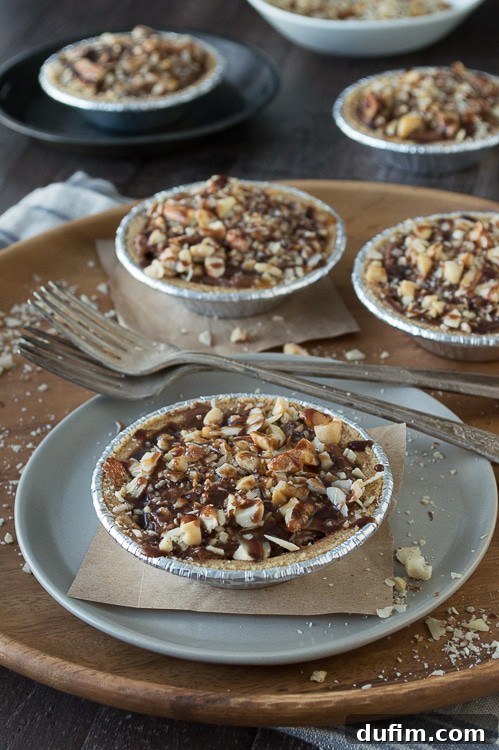 Delicious no-bake mini turtle pies featuring mixed nuts, chocolate filling, and caramel drizzle on a rustic wooden surface.